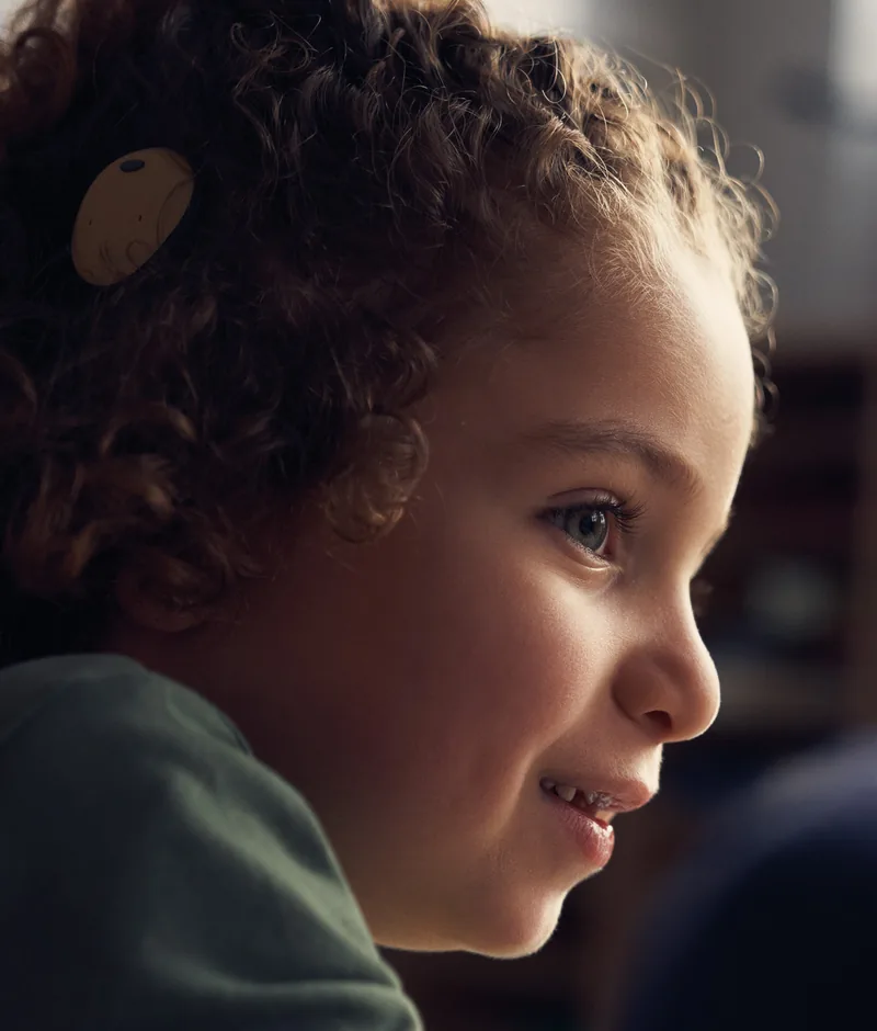 A young girl smiling, wearing a sound processor behind her ear